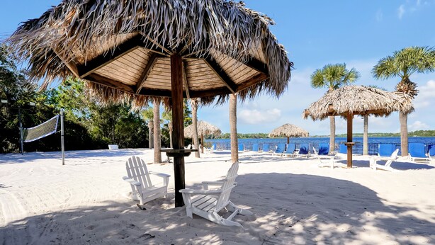 A beach with thatched umbrellas, white beach chairs, and a volleyball net. - Bahama Bay Resort - Ground Floor (Davenport)