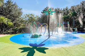 Una zona de juegos acuáticos con una fuente central, delimitada por un círculo azul y una escultura de tortuga verde.