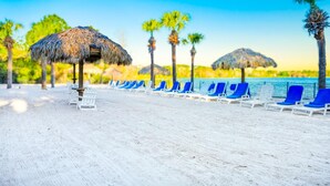 A beach with thatched umbrellas, white lounge chairs, and palm trees. - Bahama Bay Resort Penthouse w Lake View 15209 (Davenport)