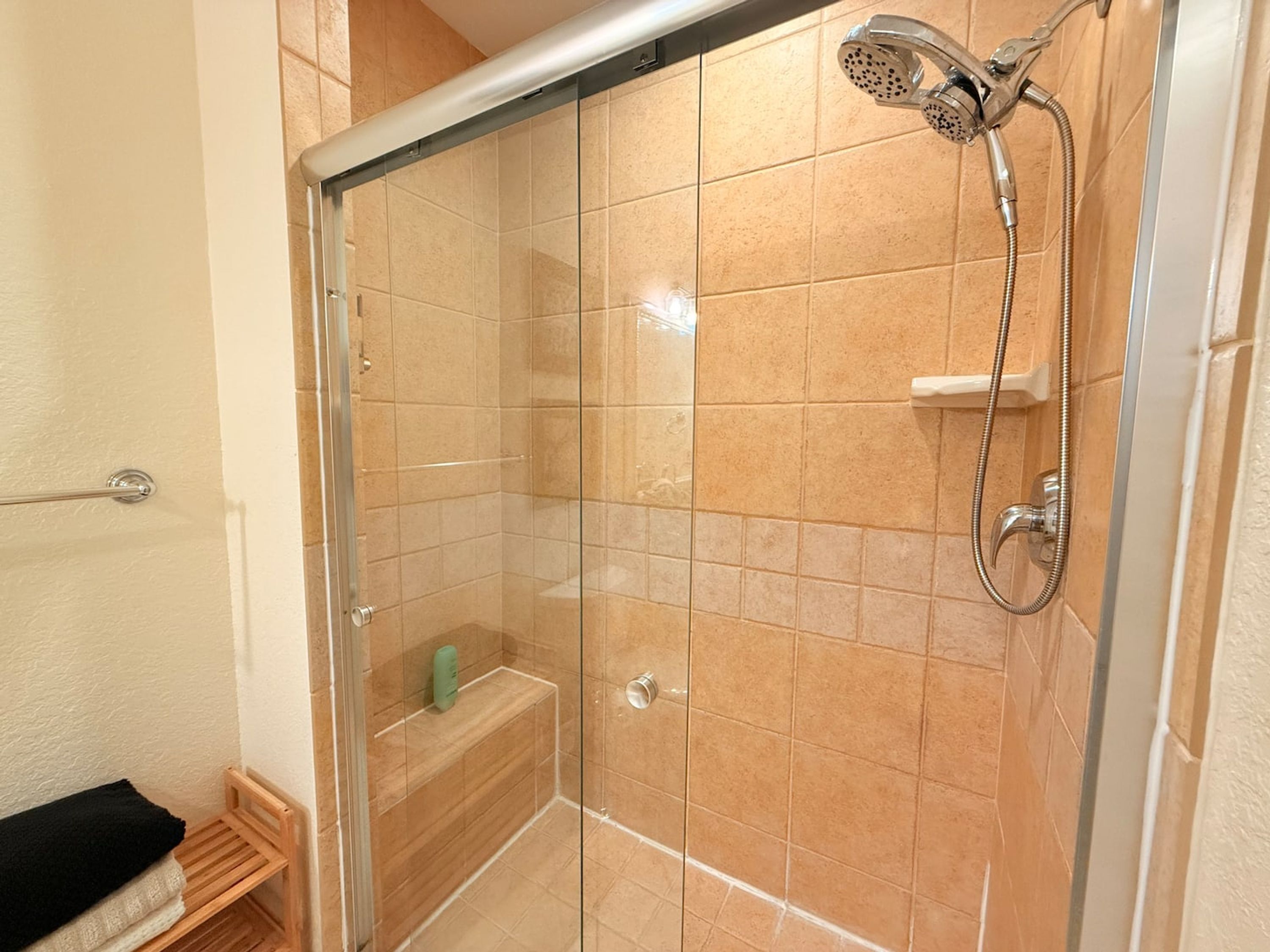 A glass-enclosed shower with a handheld showerhead and a handheld hose.