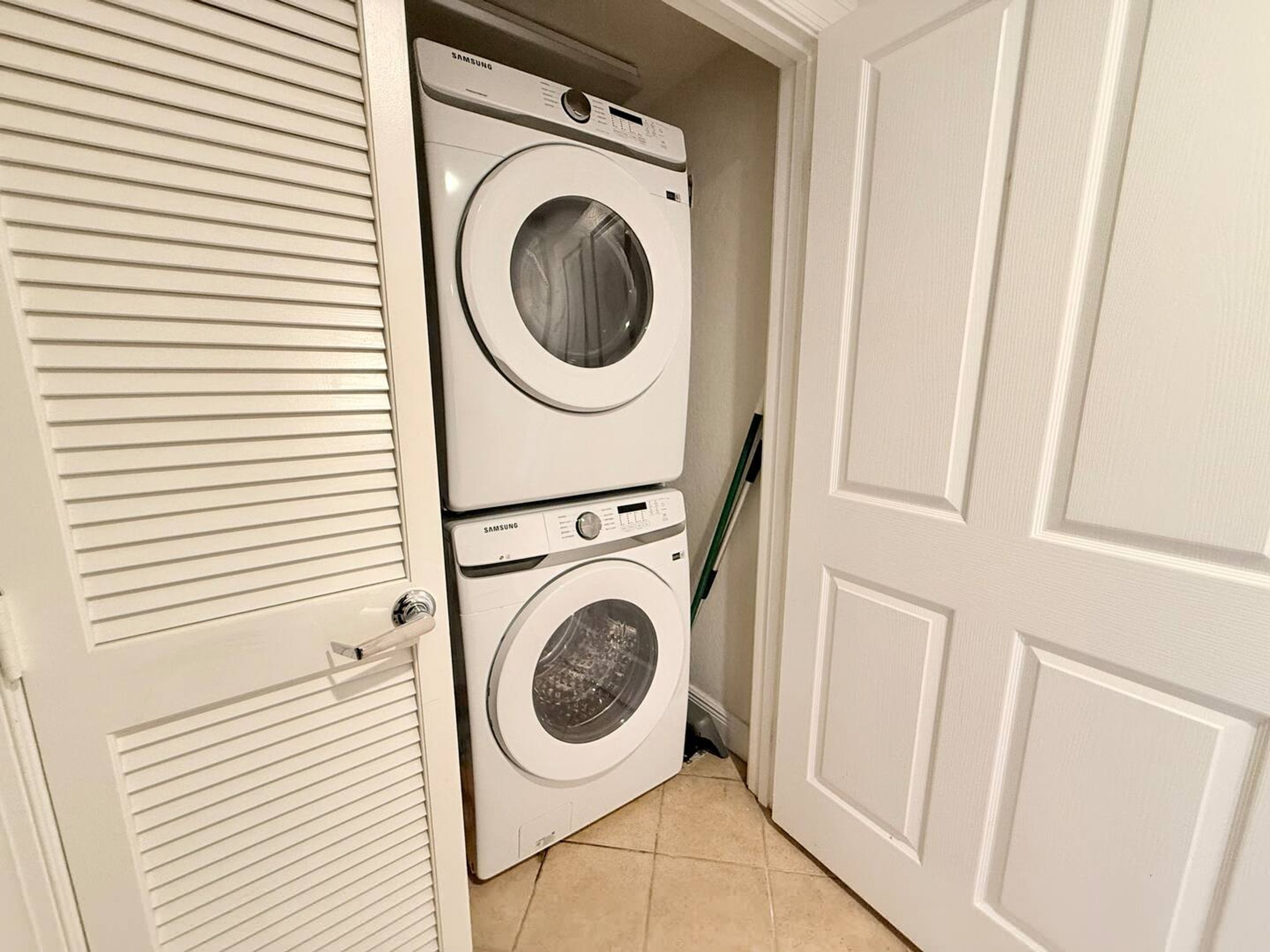 A laundry room with two stacked washers and dryers, a door, and a tiled floor.