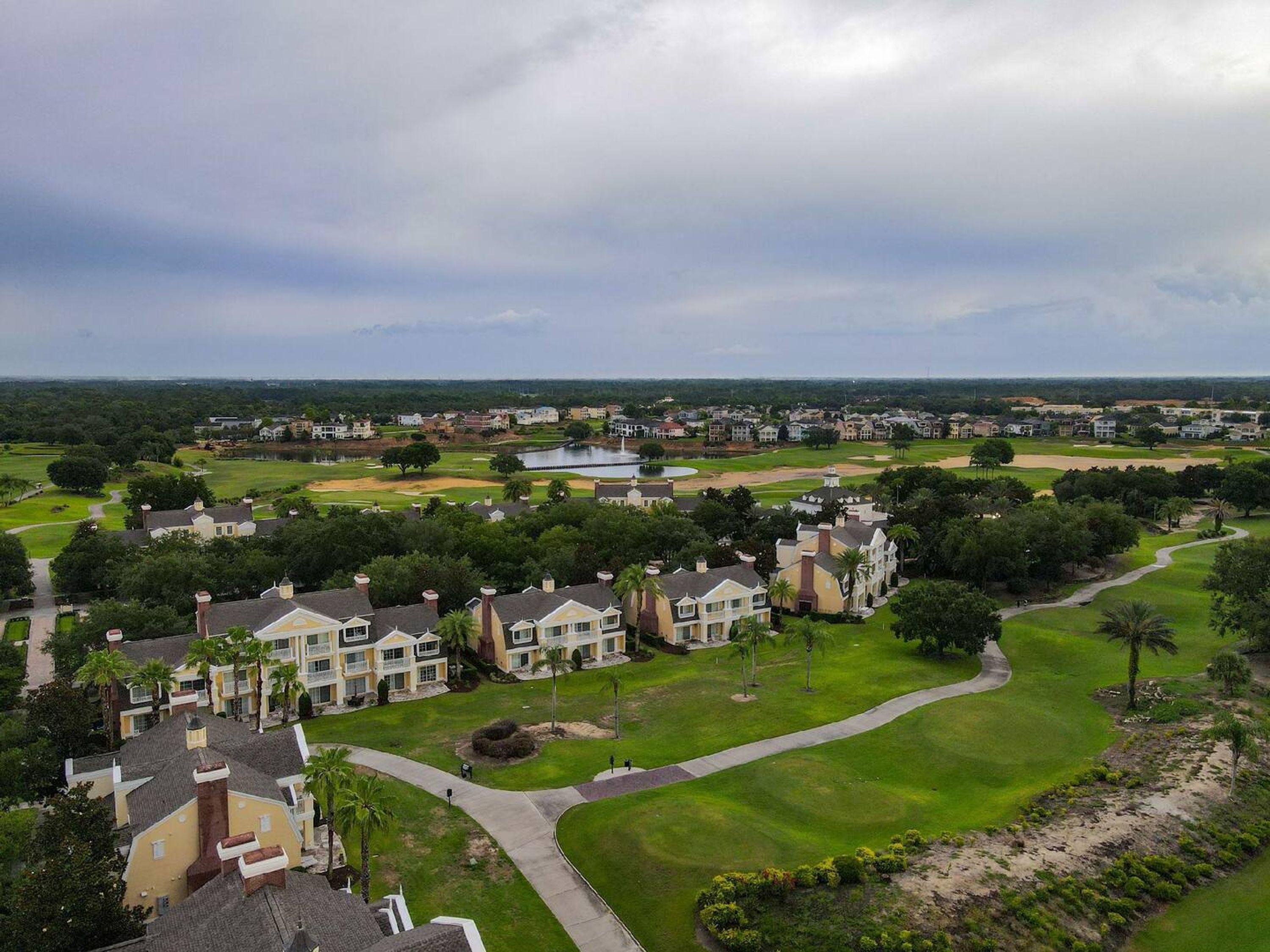 Un campo de golf con edificios residenciales, un estanque y un cielo nublado.