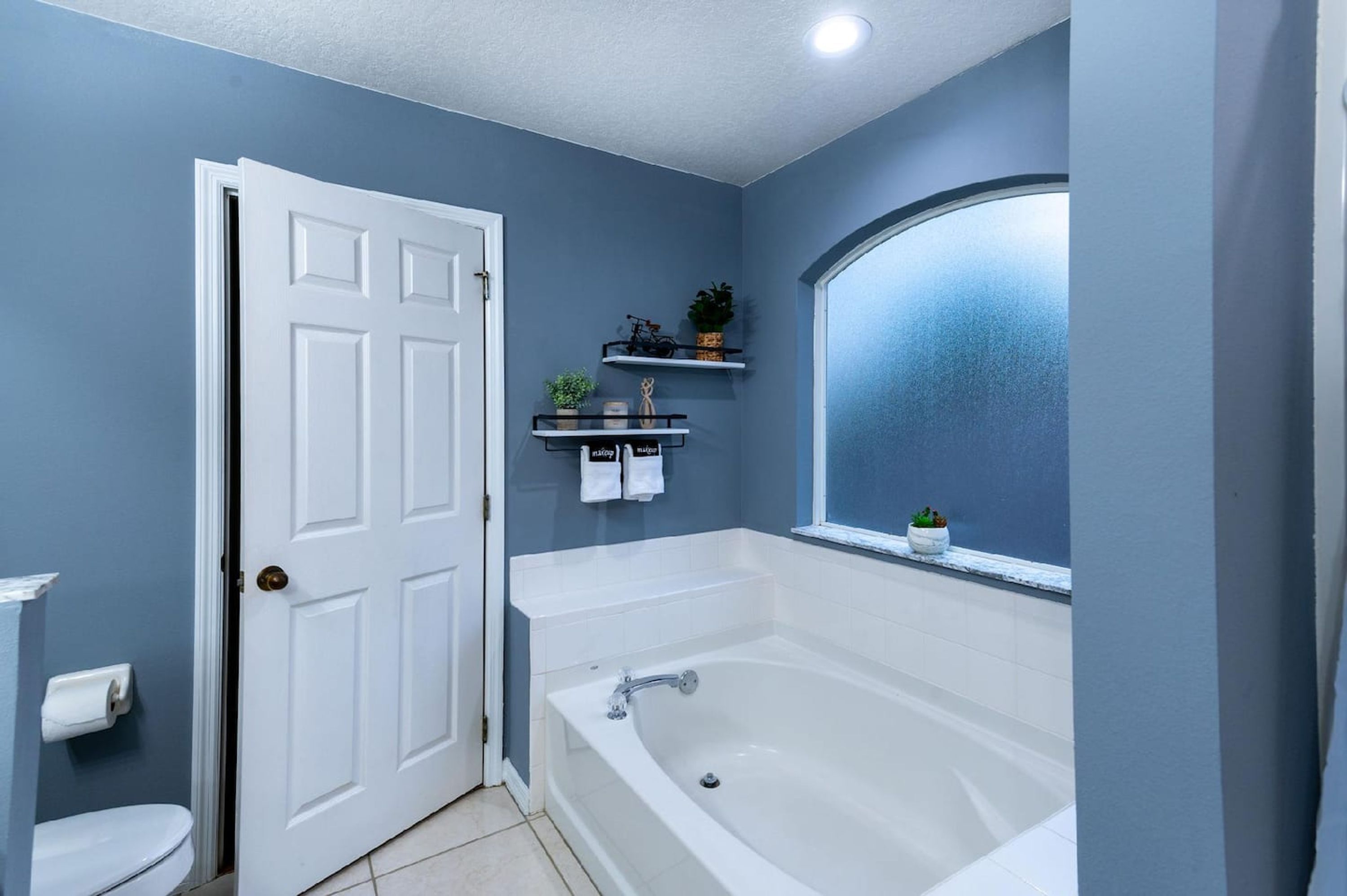 A bathroom with a white bathtub, a white door, and a window with a view.