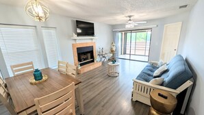 Ein geräumiges Wohnzimmer mit Kamin, eine Essecke mit Holztisch und Stühlen sowie eine gemütliche Sitzecke mit Sofa und Kissen.
