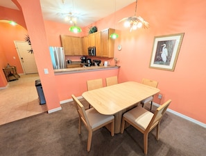 Uma sala de jantar com mesa e cadeiras de madeira, uma cozinha com armários de madeira e um quadro pendurado na parede.