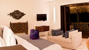 A hotel room with a bed, a sofa, a TV, a wooden headboard, a nightstand, and a balcony with a thatched roof. - Estate Venado in Punta Mita (Punta de Mita)