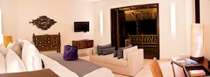 A hotel room with a bed, a sofa, a TV, a wooden headboard, a nightstand, and a balcony with a thatched roof. - Estate Venado in Punta Mita (Punta de Mita)