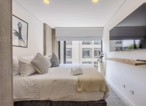 A modern hotel room with a large bed, a mounted TV, a window with a city view, and a minimalist design. - NOK Comfortable 1BR Apartment in Chico Norte (Bogotá)