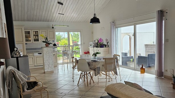 A spacious living area with a sofa, dining table, and chairs. There is a kitchen area with cabinets and a view to the outside. - Welcome to Les Renaudelles (Angles)