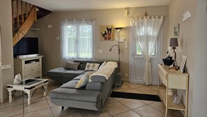 A living room with a sofa, a television, a lamp, and a staircase. - Welcome to Les Renaudelles (Angles)