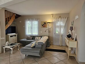 A living room with a sofa, a television, a lamp, and a staircase. - Welcome to Les Renaudelles (Angles)