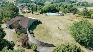 Vista aérea de una propiedad rural con una casa de piedra, piscina y campos circundantes.