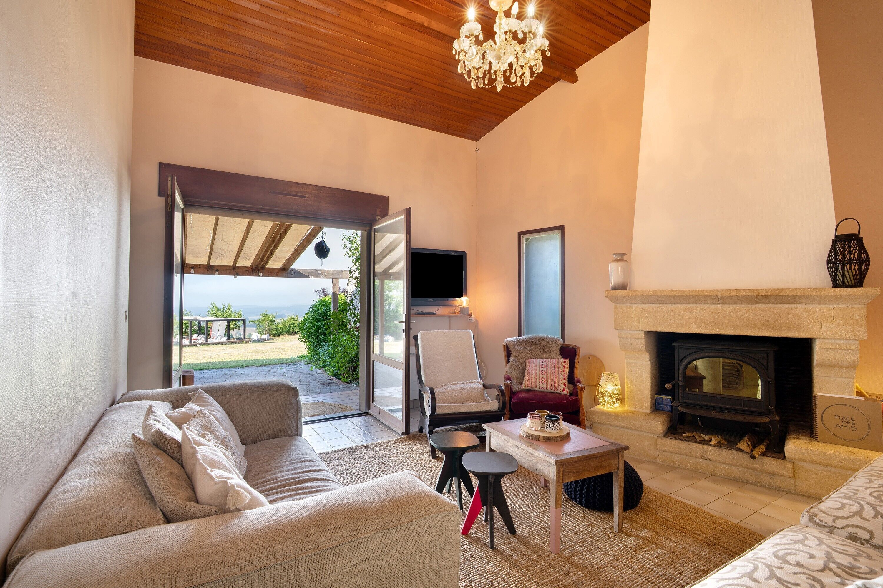 Ein gemütliches Wohnzimmer mit Kamin, einer Couch, einem Fernseher und Blick ins Freie.