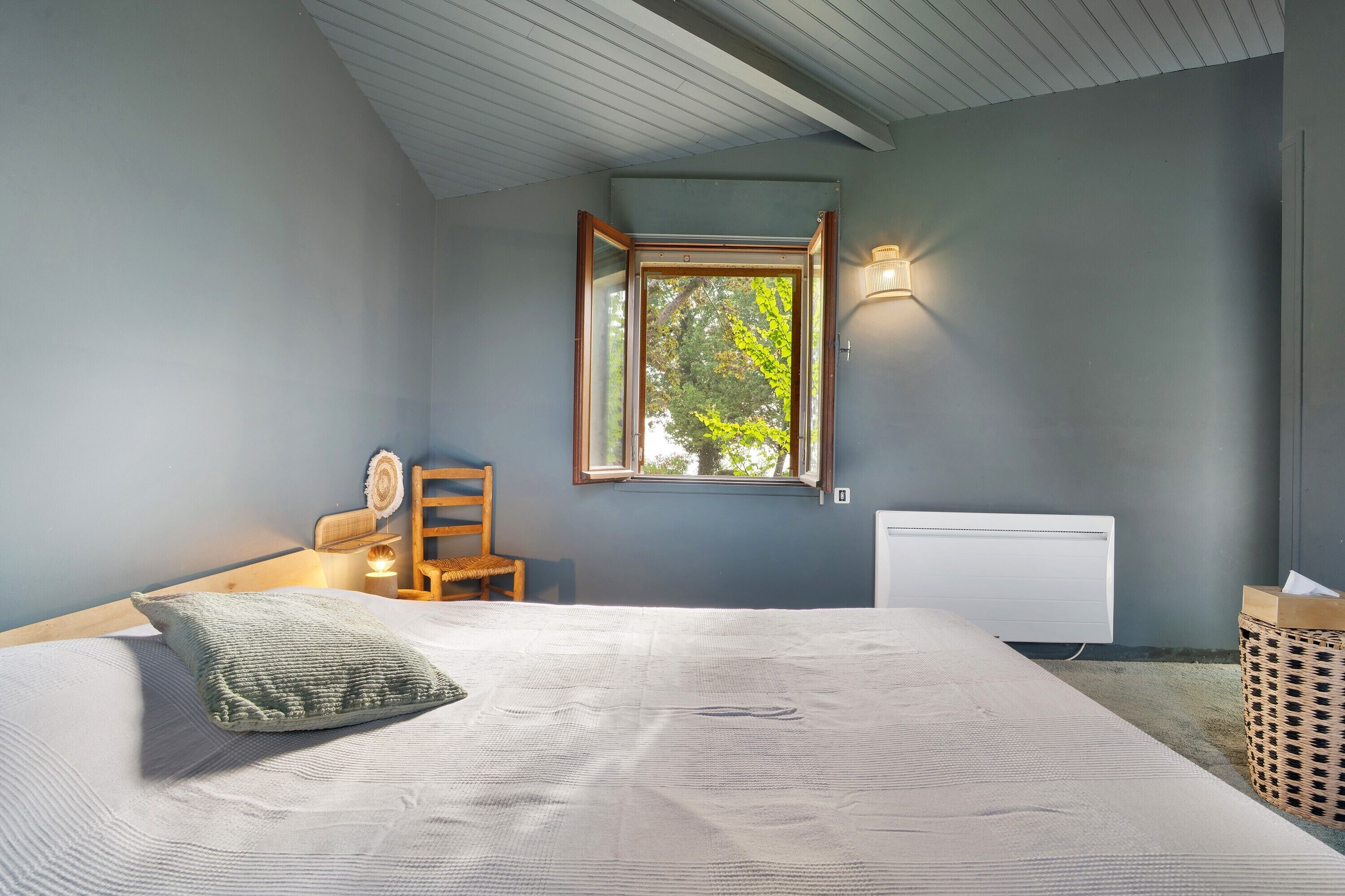 A bedroom with a bed, a window, a radiator, a chair, and a lamp.