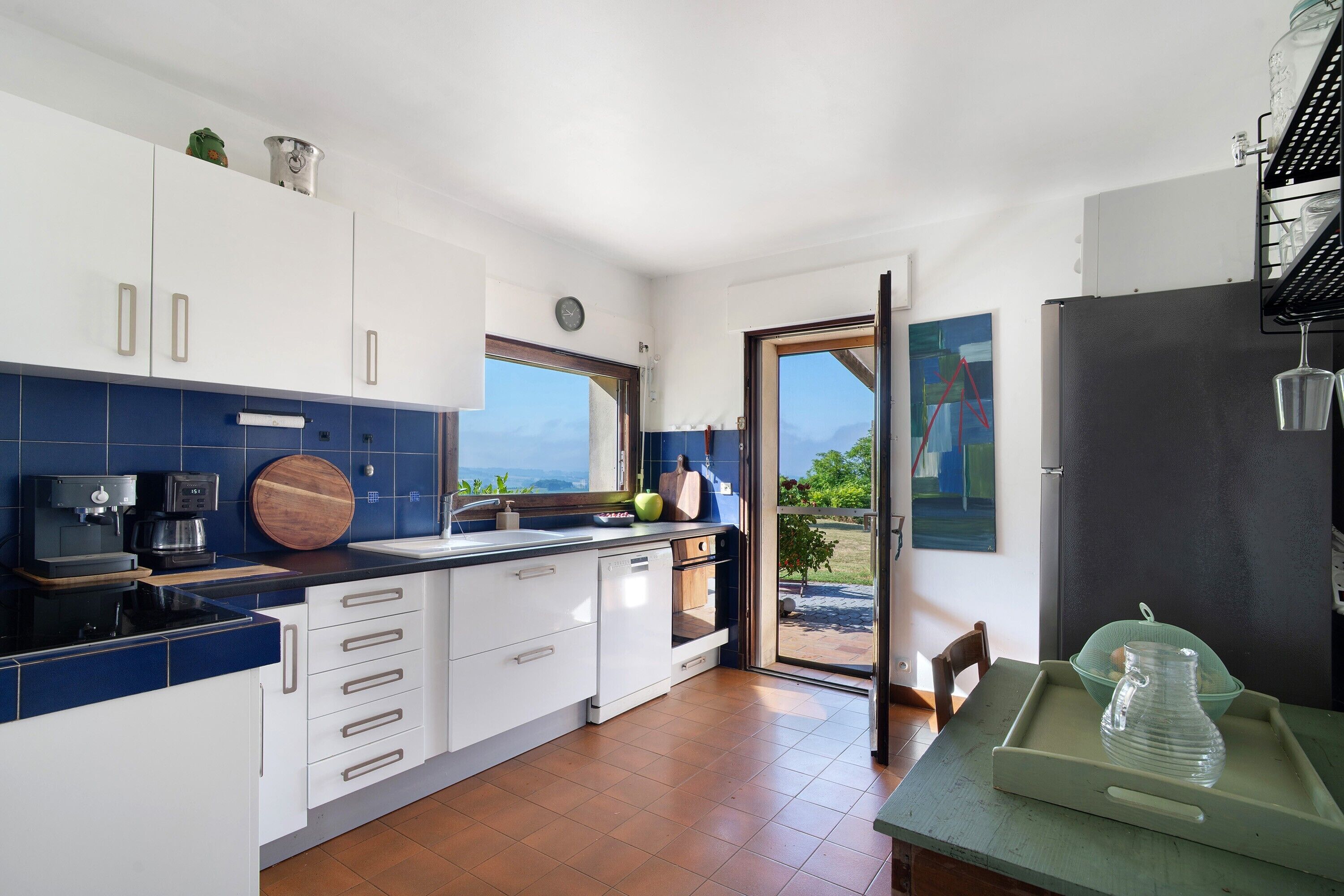 A modern kitchen with white cabinets, a coffee machine, and a view through the door.