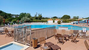 Ett poolområde med solstolar och bord, en liten pool och utsikt över landskapet.