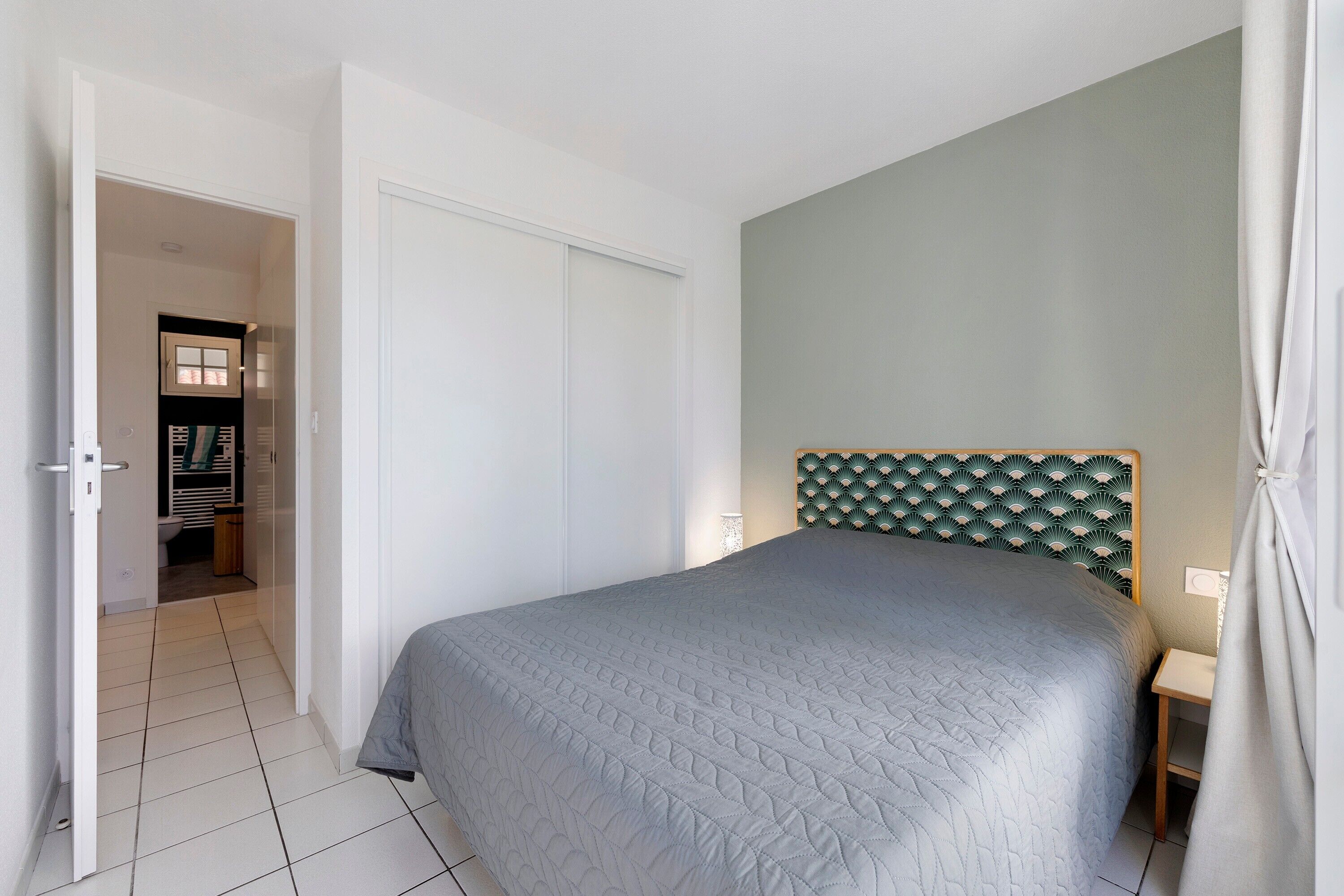 Un dormitorio con cama, puerta, mesita de noche y cabecero fijado a la pared.