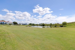 A golf course with a pond, trees, and buildings in the background. - La Terrasse du Golf Bourgenay – Spacious Apartment with Large South-Facing Terrace (Talmont-Saint-Hilaire)