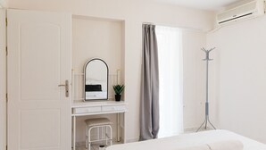 Una habitación de hotel con cama, escritorio con espejo, perchero y ventana con cortinas.