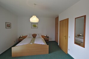 Un dormitorio con una cama de madera, mesitas de noche, una lámpara colgante, una puerta y un espejo.