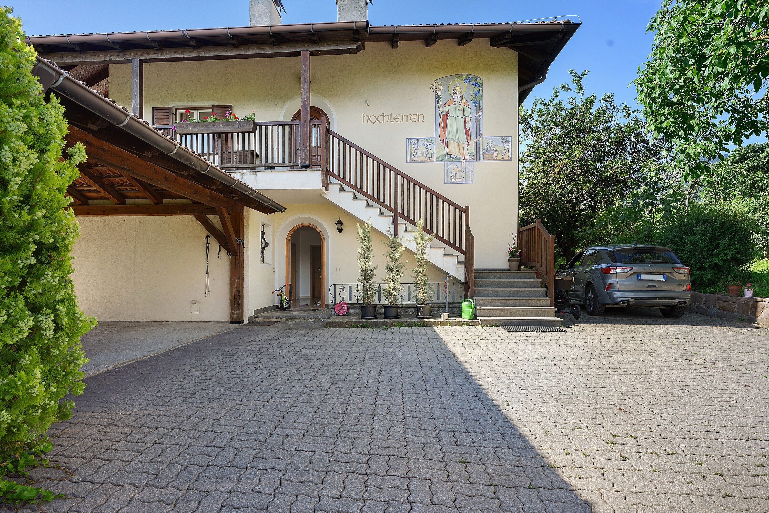 A building with a staircase leading to a balcony, a parked car, and a paved driveway.