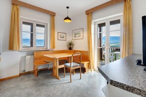 A modern kitchen with a wooden bench and table, large windows with curtains, and a view of the outdoors. - Apartment 'Weingut Hochleiten Latemar' with Mountain View, Balcony and Wi-Fi (Pianizza di Sopra)