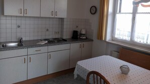 Cozinha com armários brancos, bancada de granito, cafeteira e janela com cortinas.