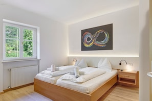 Ein Schlafzimmer mit einem Bett, einem Nachttisch, einem Wandbild, einem Fenster und einer Heizung.