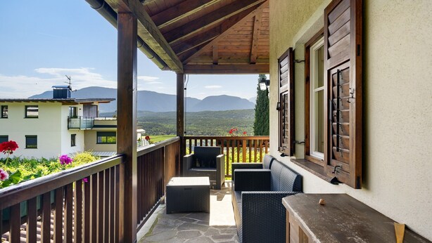 A balcony with wicker furniture, a wooden railing, and a view of mountains.