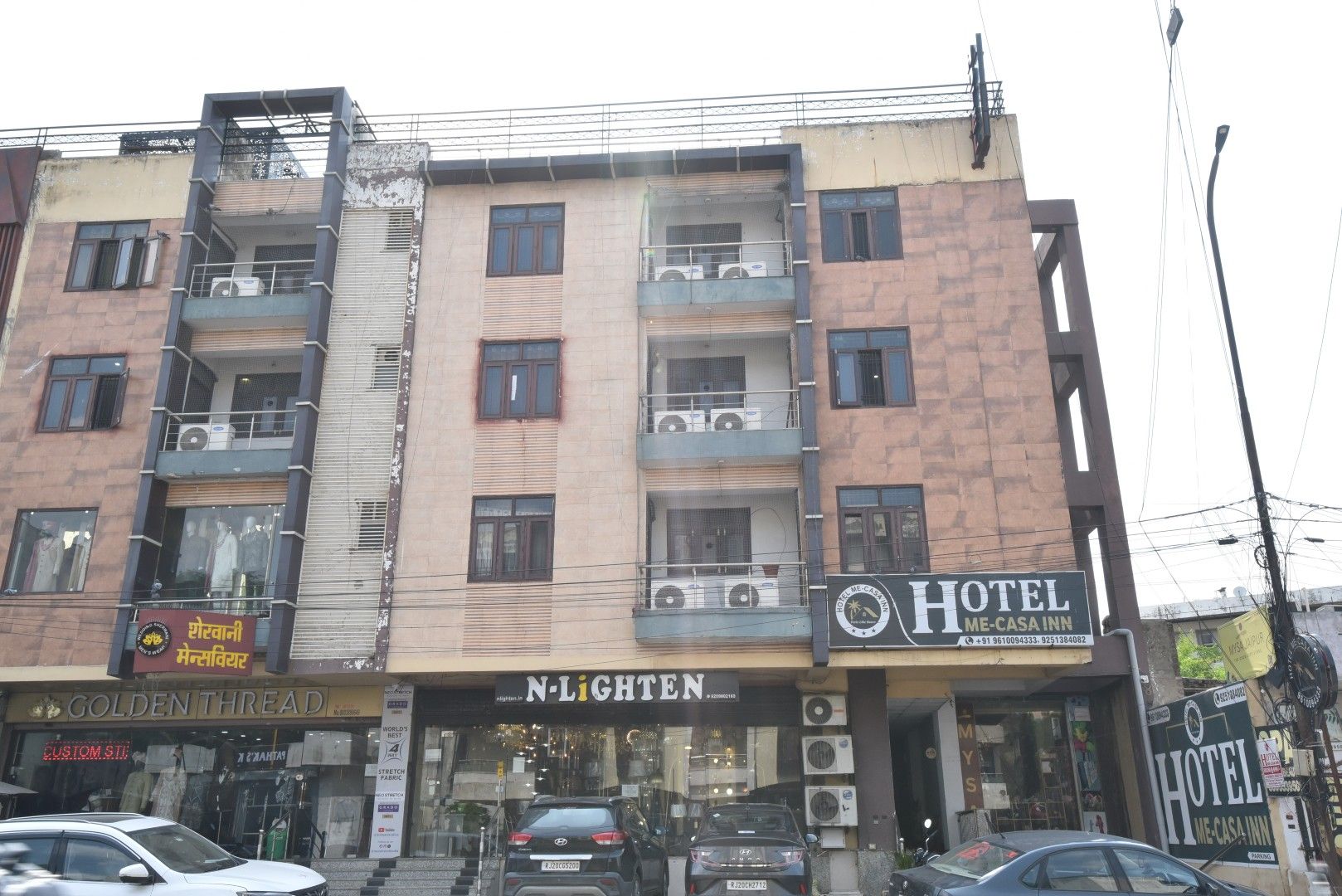 Un immeuble à plusieurs étages abritant un hôtel appelé « Hotel Me-Casa Inn » au rez-de-chaussée, avec une enseigne indiquant les coordonnées.