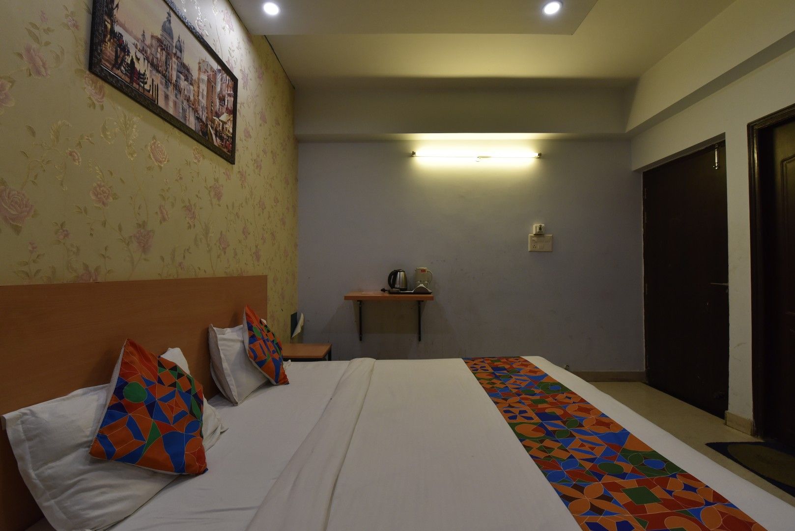 Una camera d'hotel con un letto, cuscini, un comodino, una mensola a muro e una tappezzeria decorata.