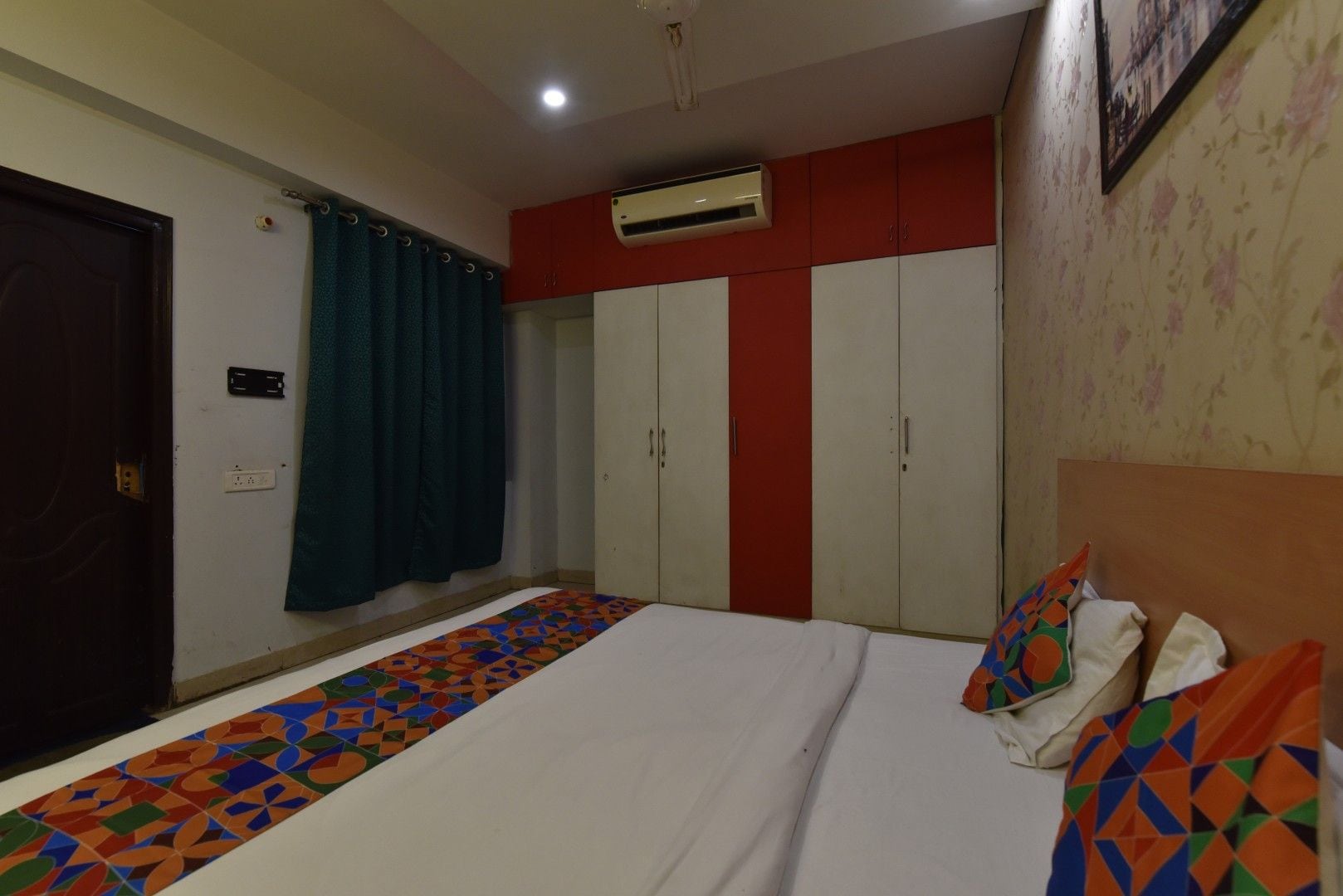 A bedroom with a bed, a wardrobe, an air conditioning unit, and a patterned floor.