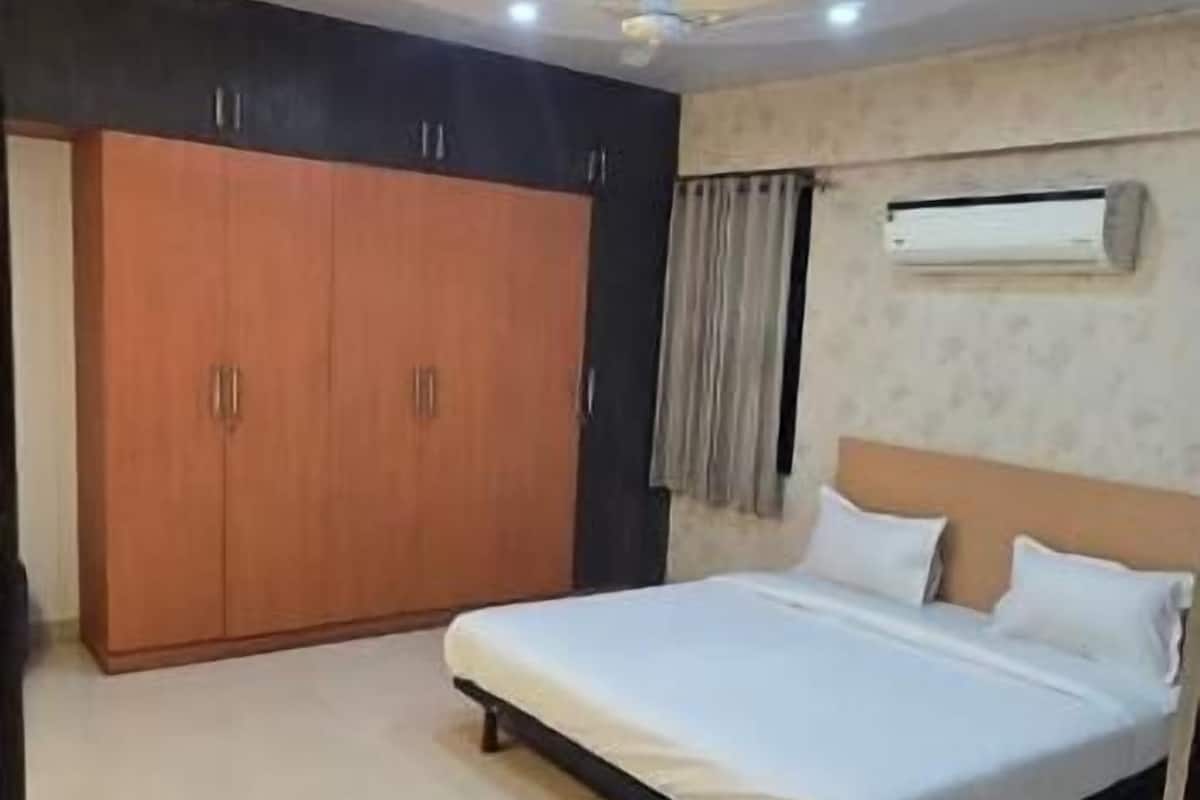 A bedroom with a bed, wardrobe, ceiling fan, and air conditioning unit.