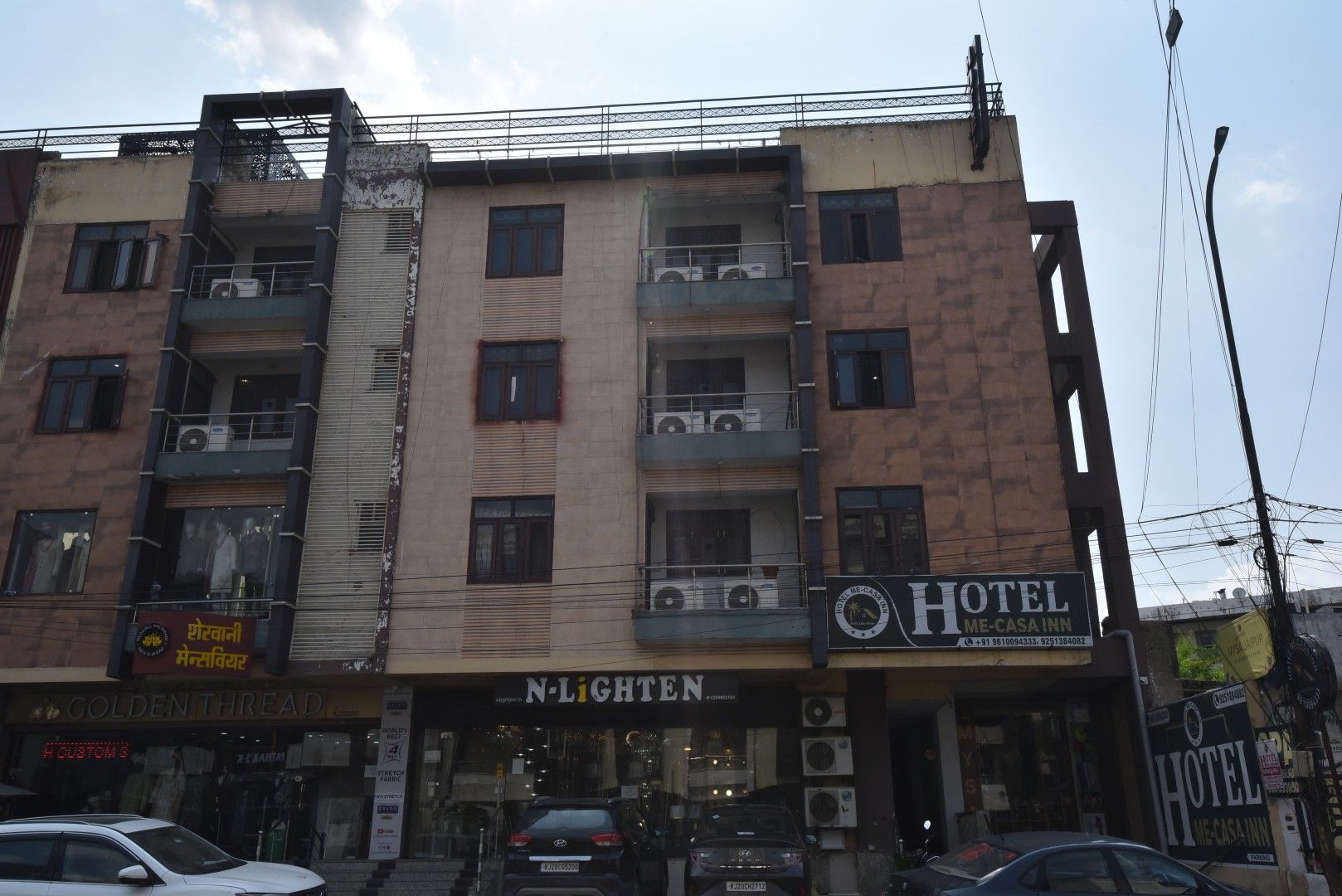 Un edificio de varios pisos con un hotel llamado 'Hotel Me-Casa Inn' en la planta baja, con balcones y unidades de aire acondicionado.