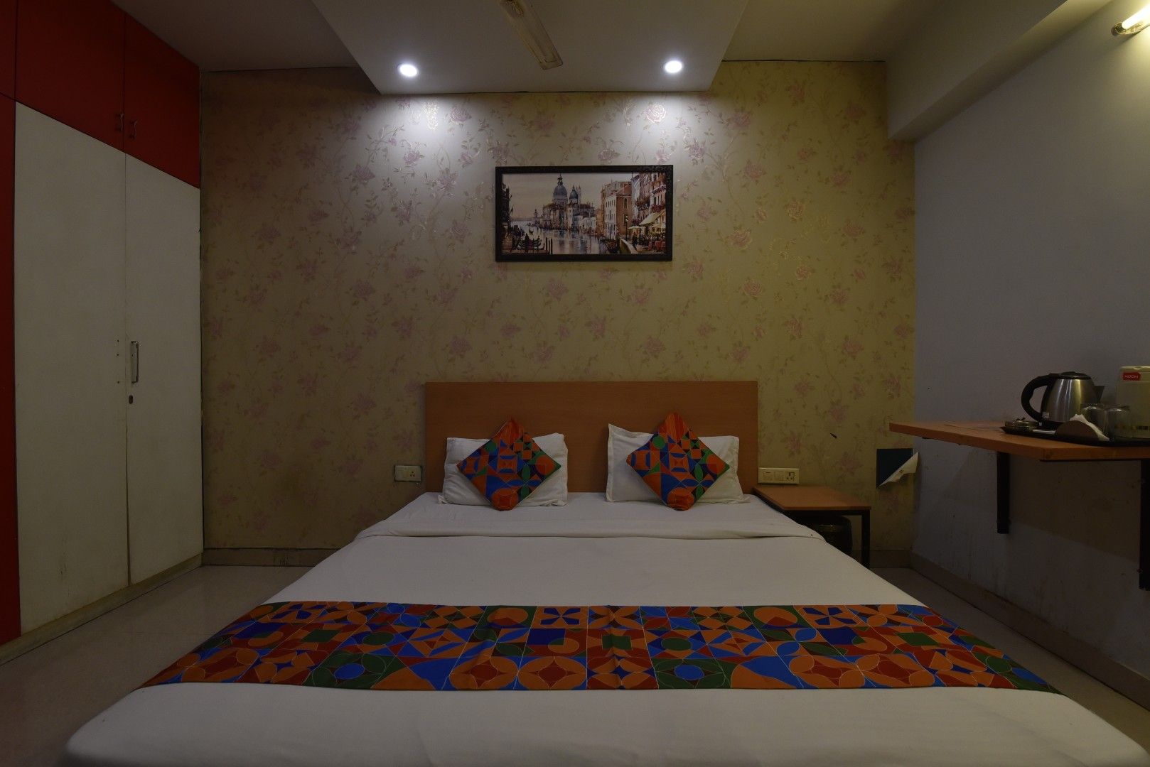 A hotel room with a bed, a nightstand, a wall-mounted picture, and a wardrobe.
