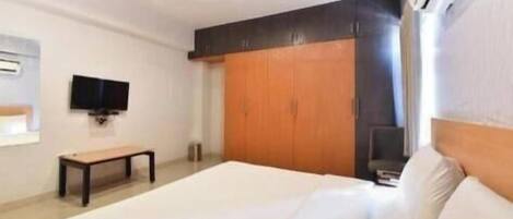 A bedroom with a bed, a wooden wardrobe, a television on the wall, and a ceiling fan.