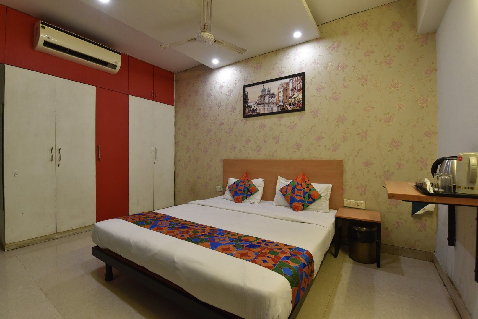A hotel room with a bed, a nightstand, a coffee maker, an air conditioning unit, and a wardrobe.