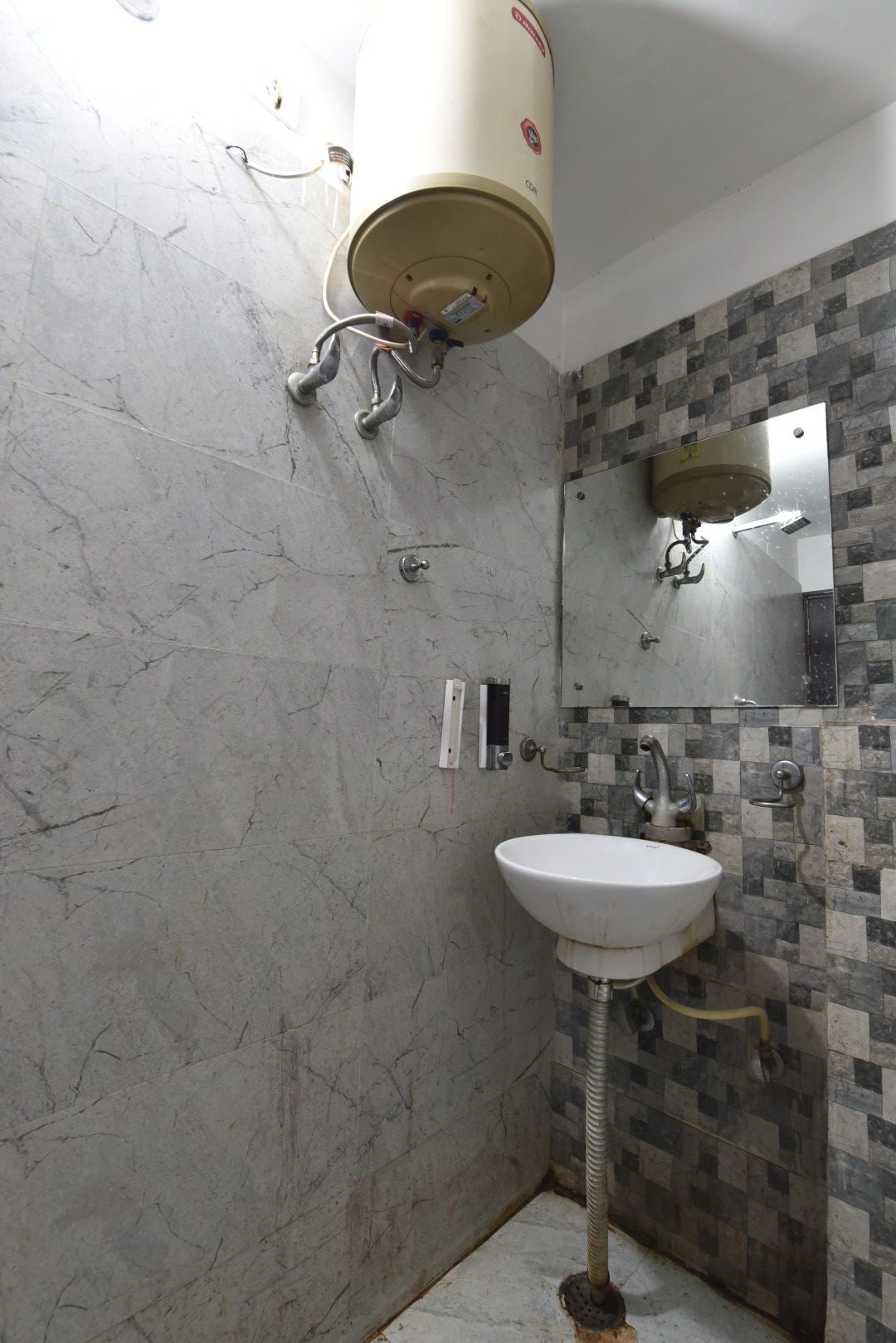 A bathroom with a marble wall, a white sink, a mirror, and a towel rack.