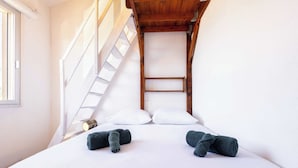 Ein Schlafzimmer mit einem Etagenbett, weißer Bettwäsche, zwei gerollten Handtüchern, einer Holzleiter und einem Fenster.