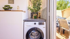 Ein kleiner Waschbereich mit Waschmaschine, einer Topfpflanze und einem Regal mit Dekoration.