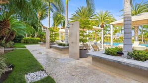 A resort pool area with palm trees, lounge chairs, and a clear blue sky. - Oceanfront 2BR Condo Le Vent 309 by Bocobay (Noord)