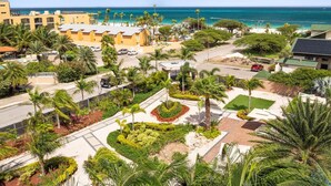 A coastal resort with a view of the ocean, featuring palm trees, a parking area, and a building with a flat roof. - Oceanfront 2BR Condo Le Vent 309 by Bocobay (Noord)