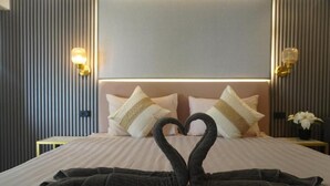 Ein Hotelzimmer mit Bett, Kissen, Wandleuchten und einer Herz-förmigen Handtuchgestaltung.
