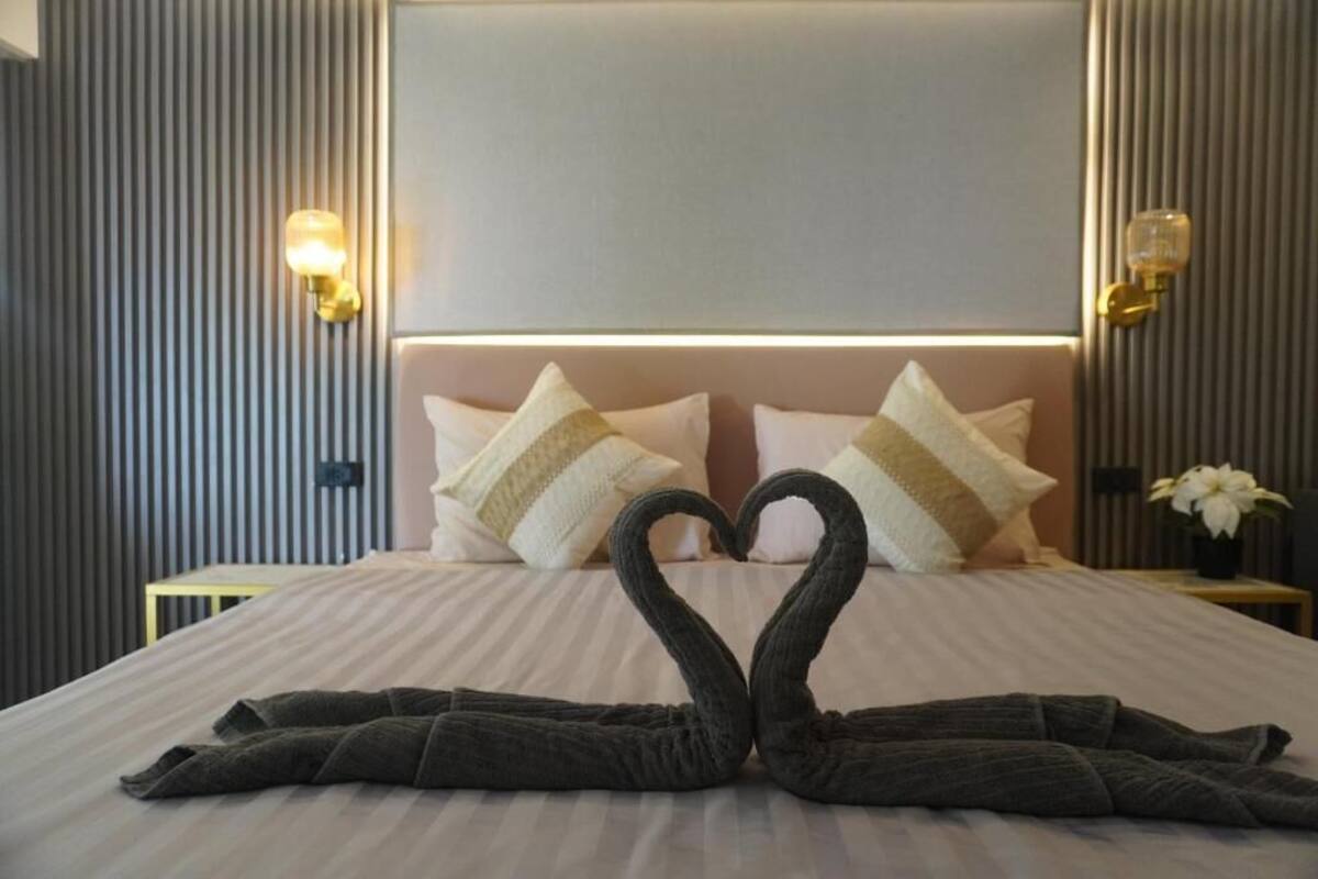 Une chambre d’hôtel avec un lit, des oreillers, des appliques murales et une disposition originale des serviettes en forme de cœur.