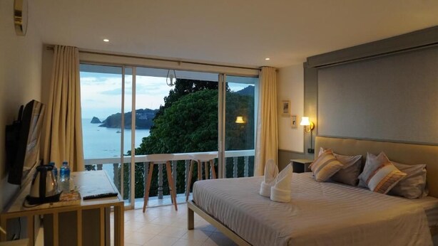 Ein Hotelzimmer mit einem großen Bett, einem Schreibtisch mit Stuhl, Meerblick und einem Balkon.