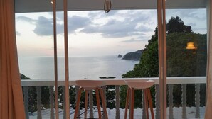 Ein Balkon mit Tisch und Stühlen, der Blick auf die Küste mit Bäumen und dem Meer bietet.