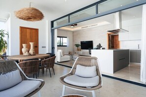 Ein modernes Interieur mit Essbereich, Korbstühlen, einer Küche mit Fernseher und einem großen Fenster.
