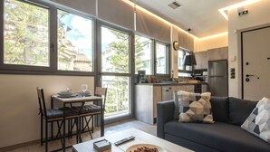 Un salon moderne avec un canapé, une table à manger et des chaises. On aperçoit une cuisine à l’arrière-plan, avec un réfrigérateur et une cuisinière.