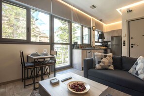 A modern living room with a sofa, dining table, and chairs. A kitchen is visible in the background with a refrigerator and stove. - Luxury Haven in the most ideal area of Athens 2 (Athina)