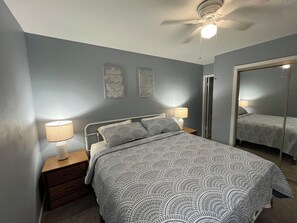A bedroom with a bed, two bedside lamps, a ceiling fan, a mirror, and a door. - 2BR Condo,Pools & Walk to Beach (Ocean City)
